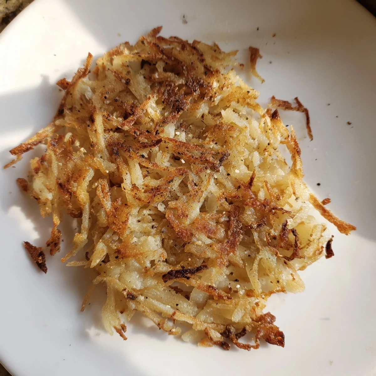 Sizzling in the skillet, freshly made crispy hash browns with a lovely, golden exterior ready to eat.