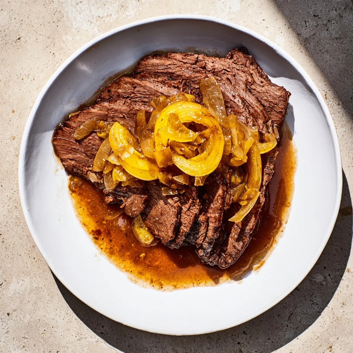 Tender, glistening braised brisket with onions, aromatic from slow-cooking, served with rich, savory pan sauce.
