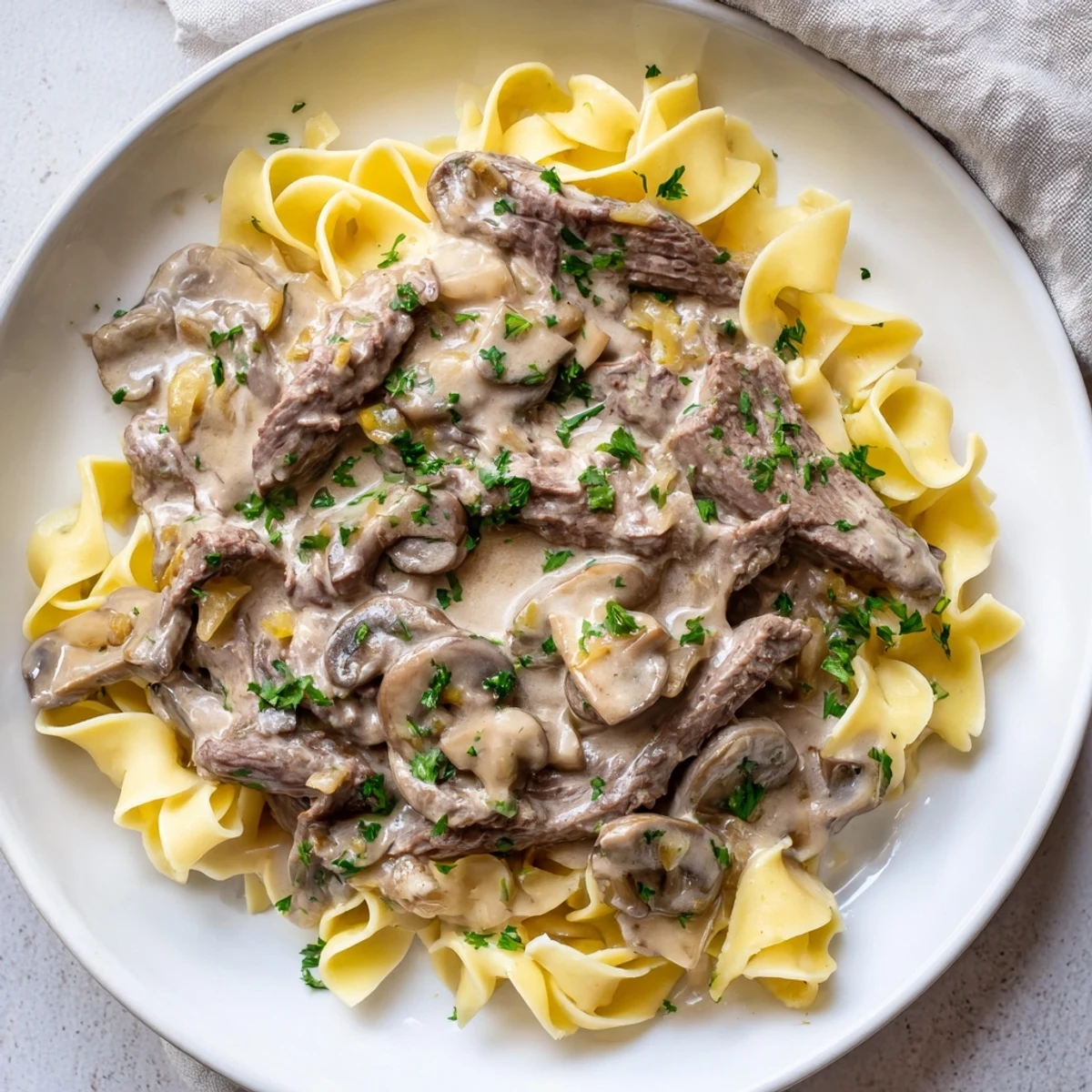 Tender beef stroganoff with creamy mushroom sauce over golden, buttery egg noodles, ready to eat.
