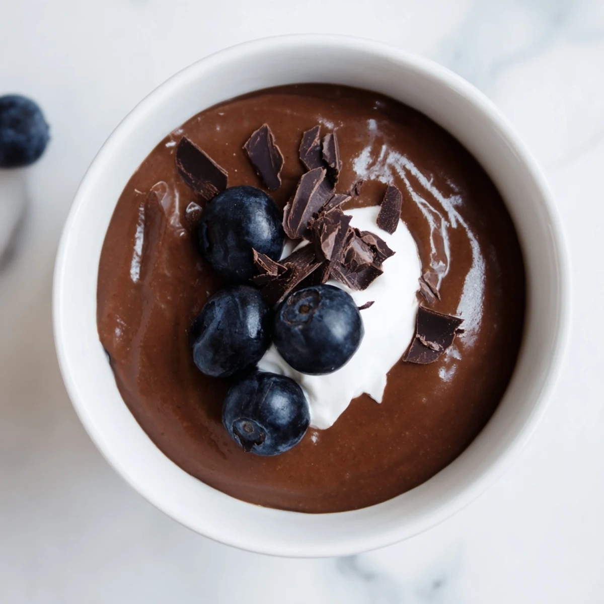 Smooth, dark chocolate avocado pudding in a glass ready to be enjoyed with a spoon.