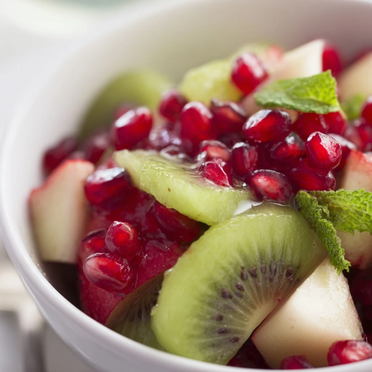 Vibrant Winter Fruit Salad with Pomegranate and Lime in a white bowl with fresh mint garnish.