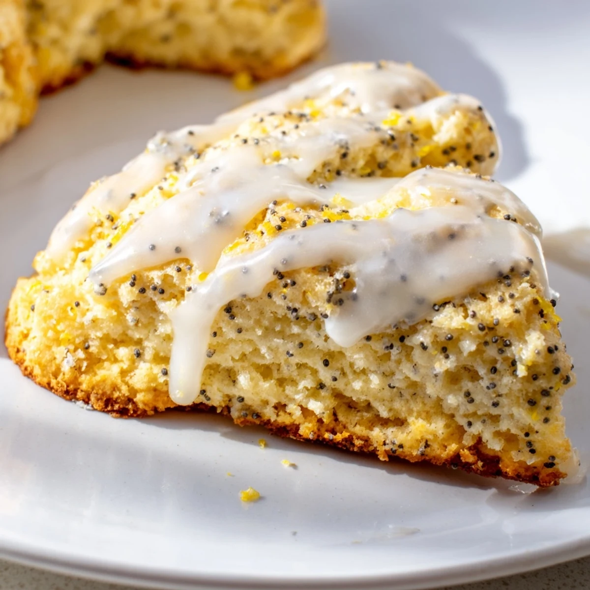 Close-up of a halved Lemon Poppy Seed Scone showing a tender, buttery crumb studded with poppy seeds and dripping with sweet citrus glaze.