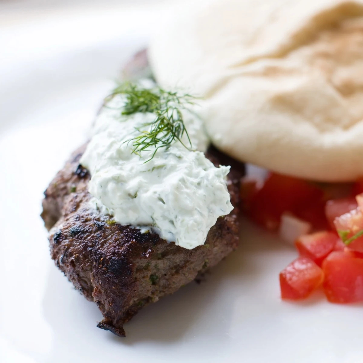 Golden-brown, spiced Beef Kofta Kebabs with Tzatziki Sauce resting beside lemon wedges and fresh herbs on a rustic table.