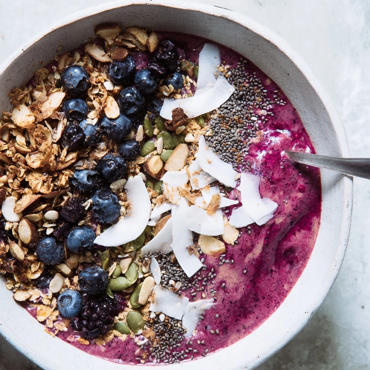 Overhead view of a Winter Berry Smoothie Bowl with thick purple smoothie and generous granola, seeds, and berries.