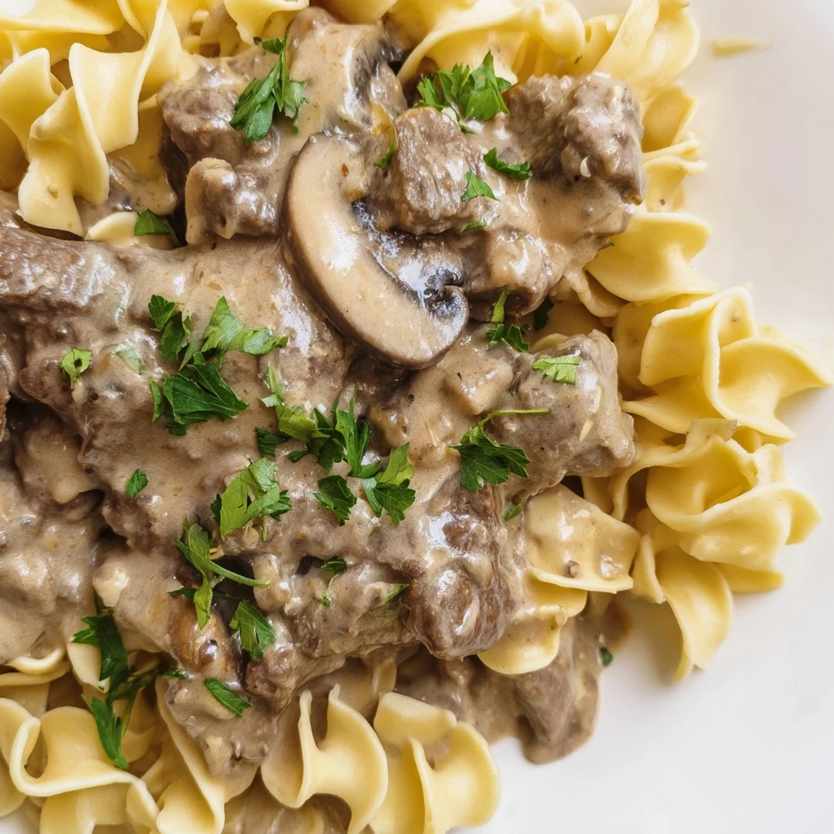 Hearty Beef Stroganoff over egg noodles plated with sautéed mushrooms and savory sauce.