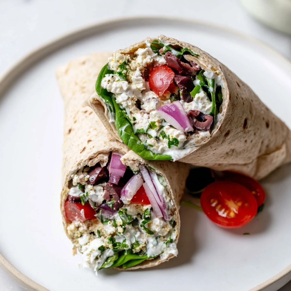 Freshly assembled Mediterranean Wrap with Feta and Olives, filled with crisp vegetables and drizzled with creamy herbed yogurt sauce on a wooden board.