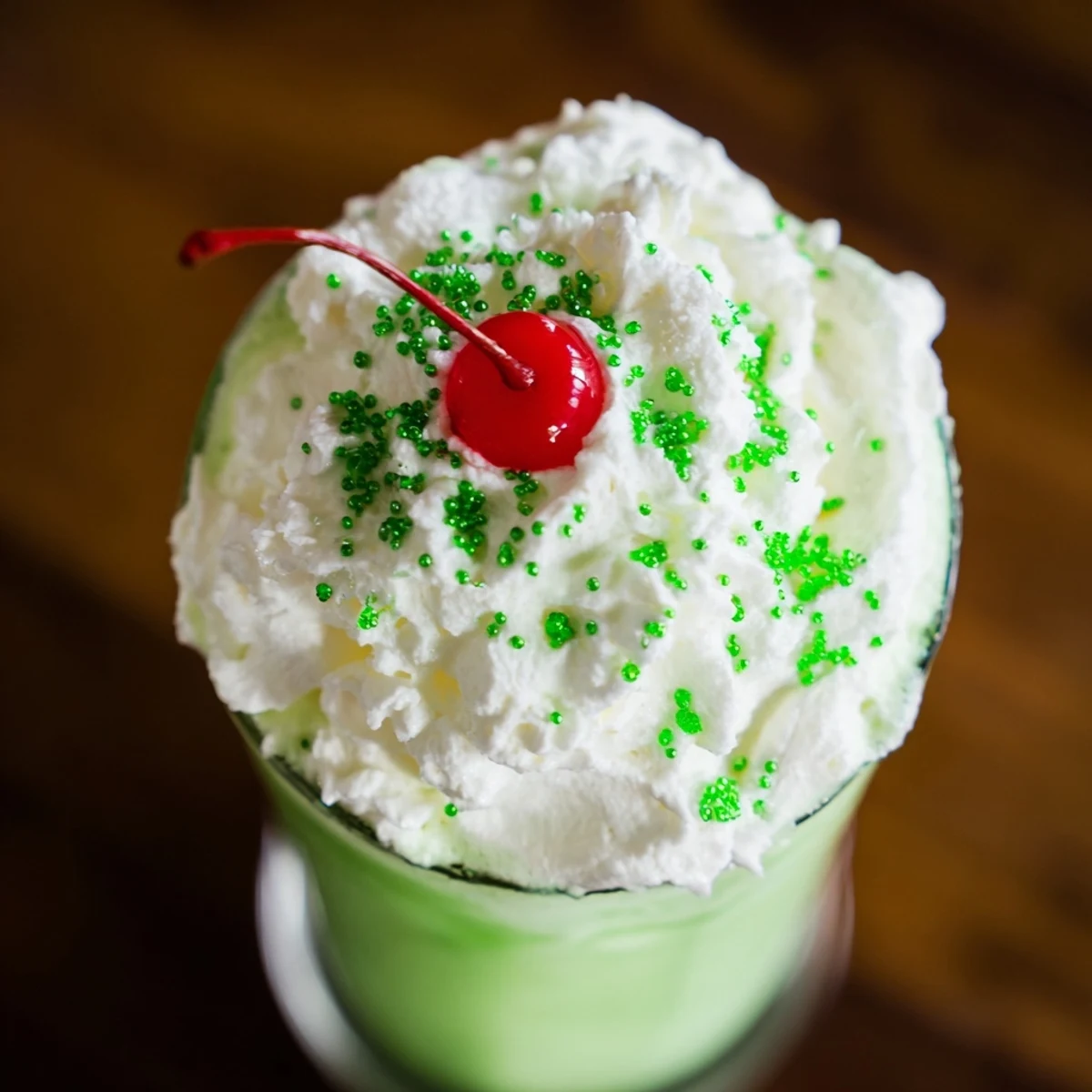 A tall glass of homemade Shamrock Shake with whipped cream, garnished with green sprinkles and a maraschino cherry for a festive St. Patrick's Day treat.