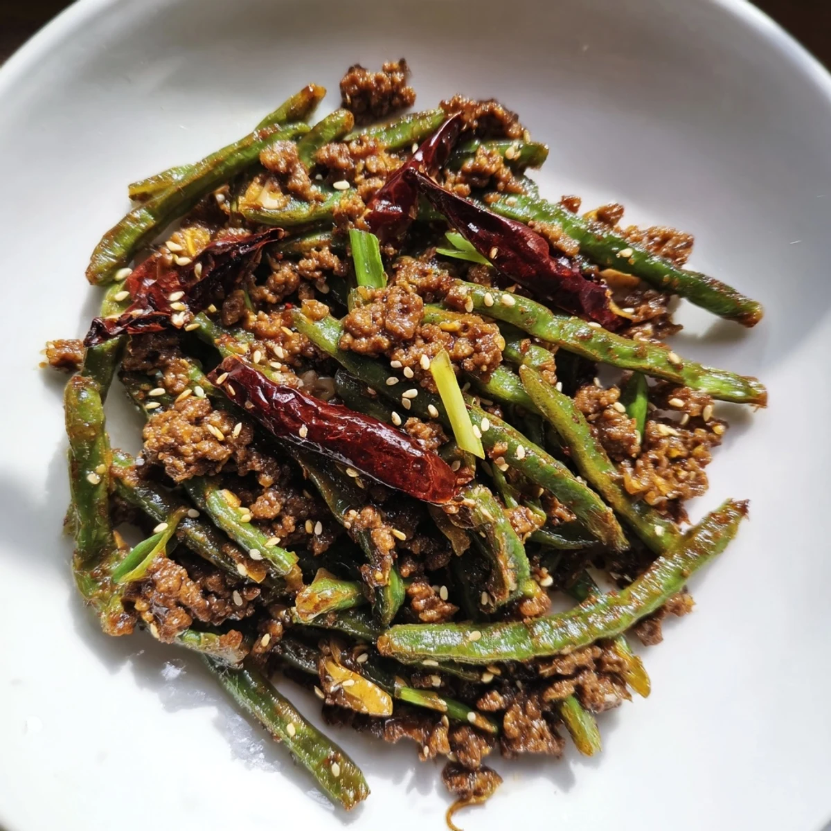 A close-up of spicy Szechuan green beans with minced beef, glistening with sauce and flecked with dried chilies for bold flavor.  