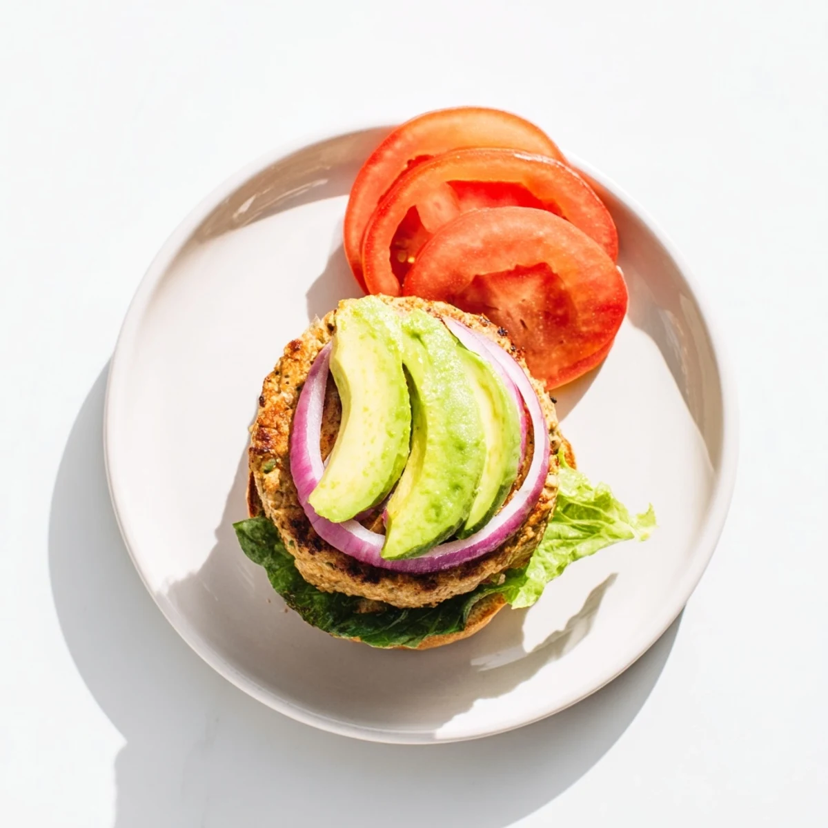 Plated turkey burger with avocado and tomato, served alongside sweet potato fries on a rustic table.
