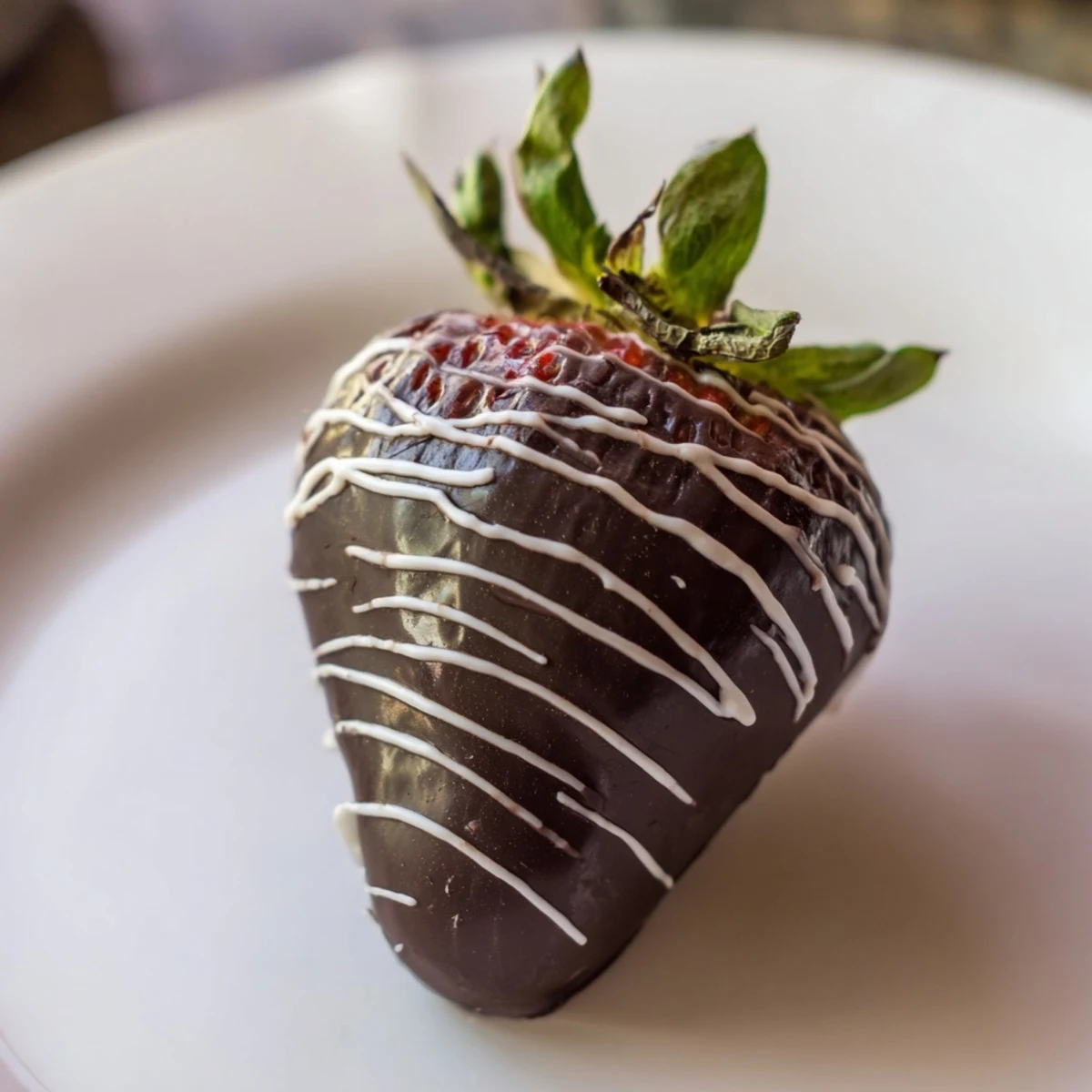 Homemade chocolate dipped strawberries with white chocolate drizzle garnished with crushed nuts, placed on parchment paper for a sweet treat.