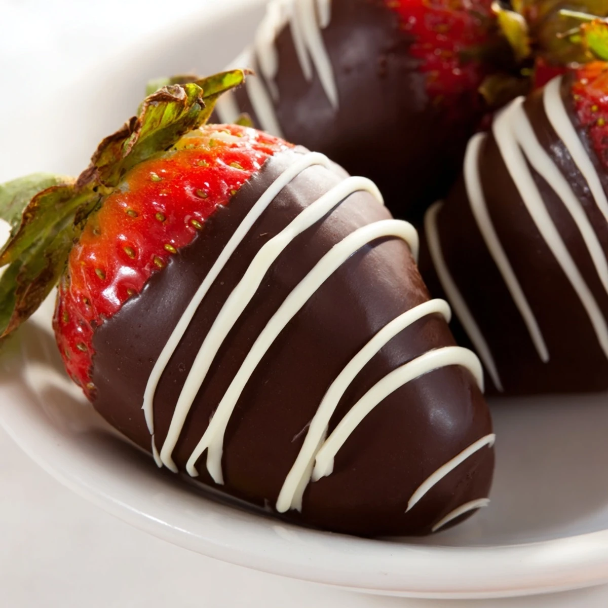 Freshly dipped strawberries in glossy dark chocolate with an elegant white drizzle, arranged on a parchment-lined tray for a romantic dessert treat.
