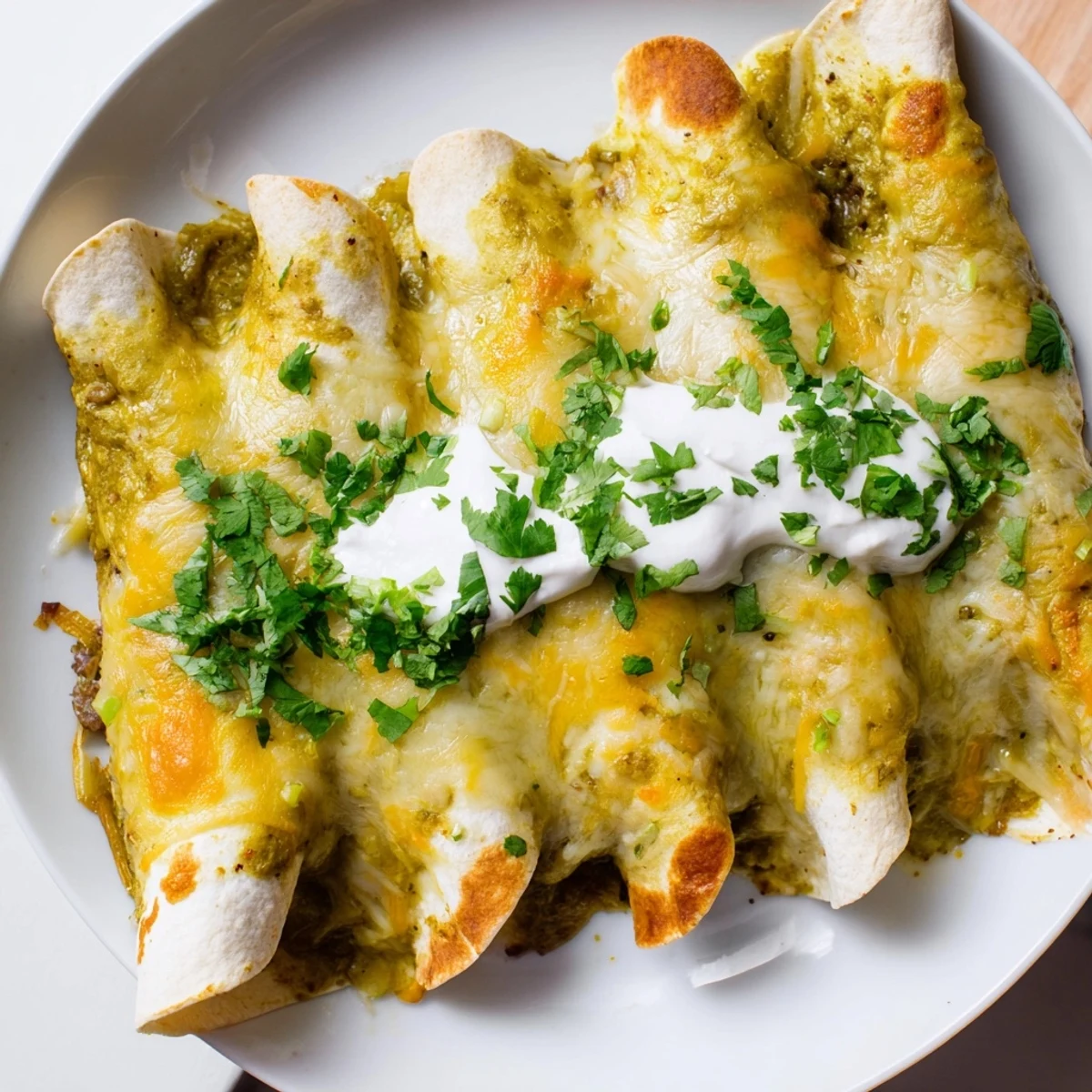 A single serving of Beef Enchiladas with Green Sauce is plated, topped with sour cream and cilantro, ready to be enjoyed for a comforting dinner.