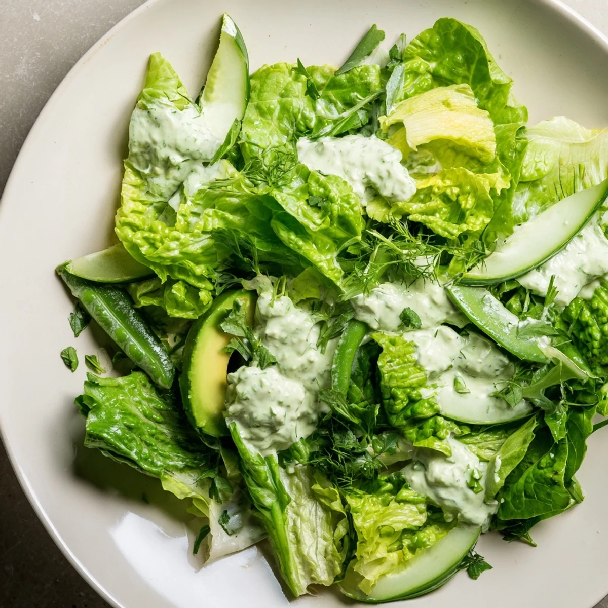 Freshly made Green Salad with Green Goddess Dressing with creamy green sauce and sliced avocado on crisp greens.