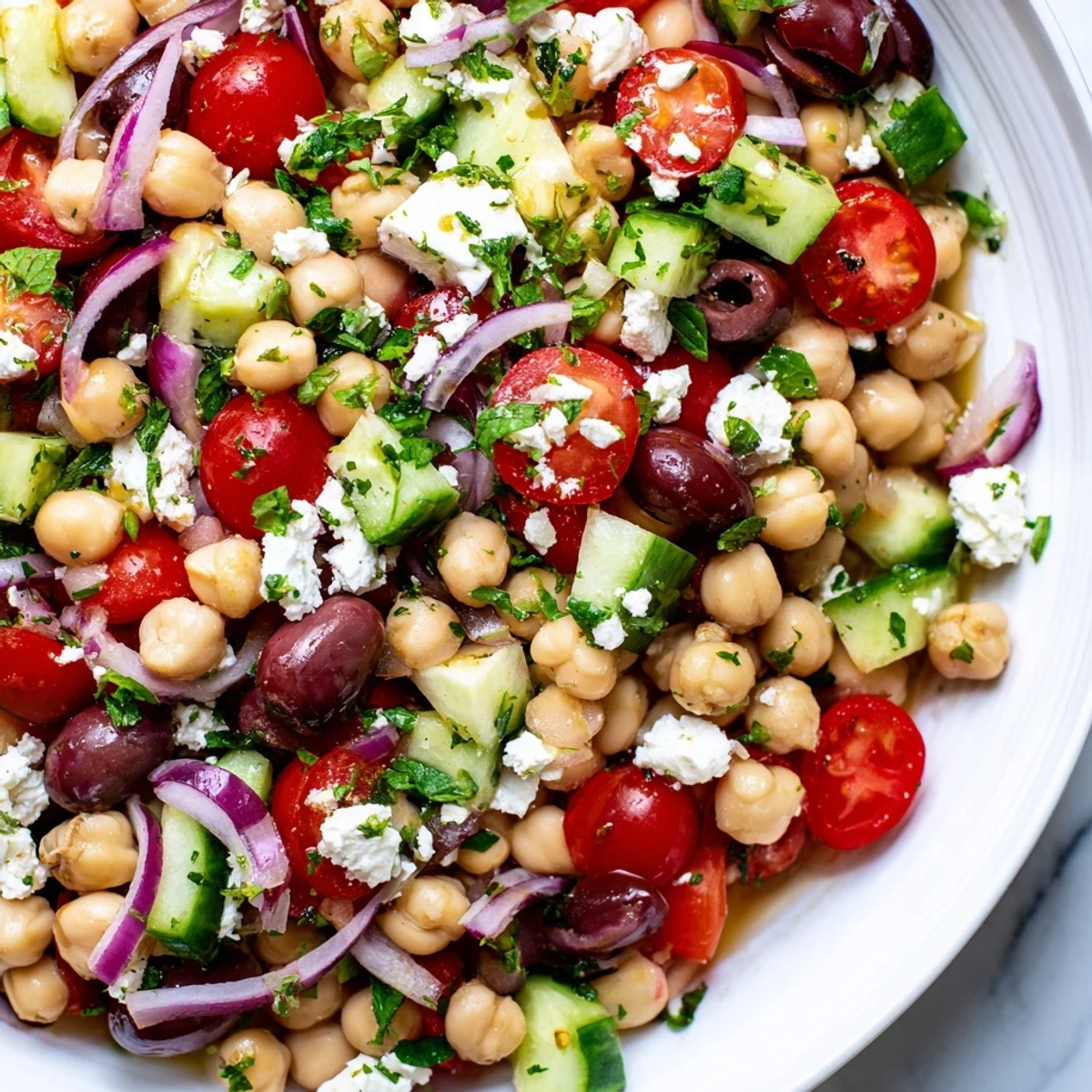 Colorful Mediterranean Dense Bean Salad in a white bowl with chickpeas, kidney beans, cucumber, tomatoes, and crumbled feta cheese.
