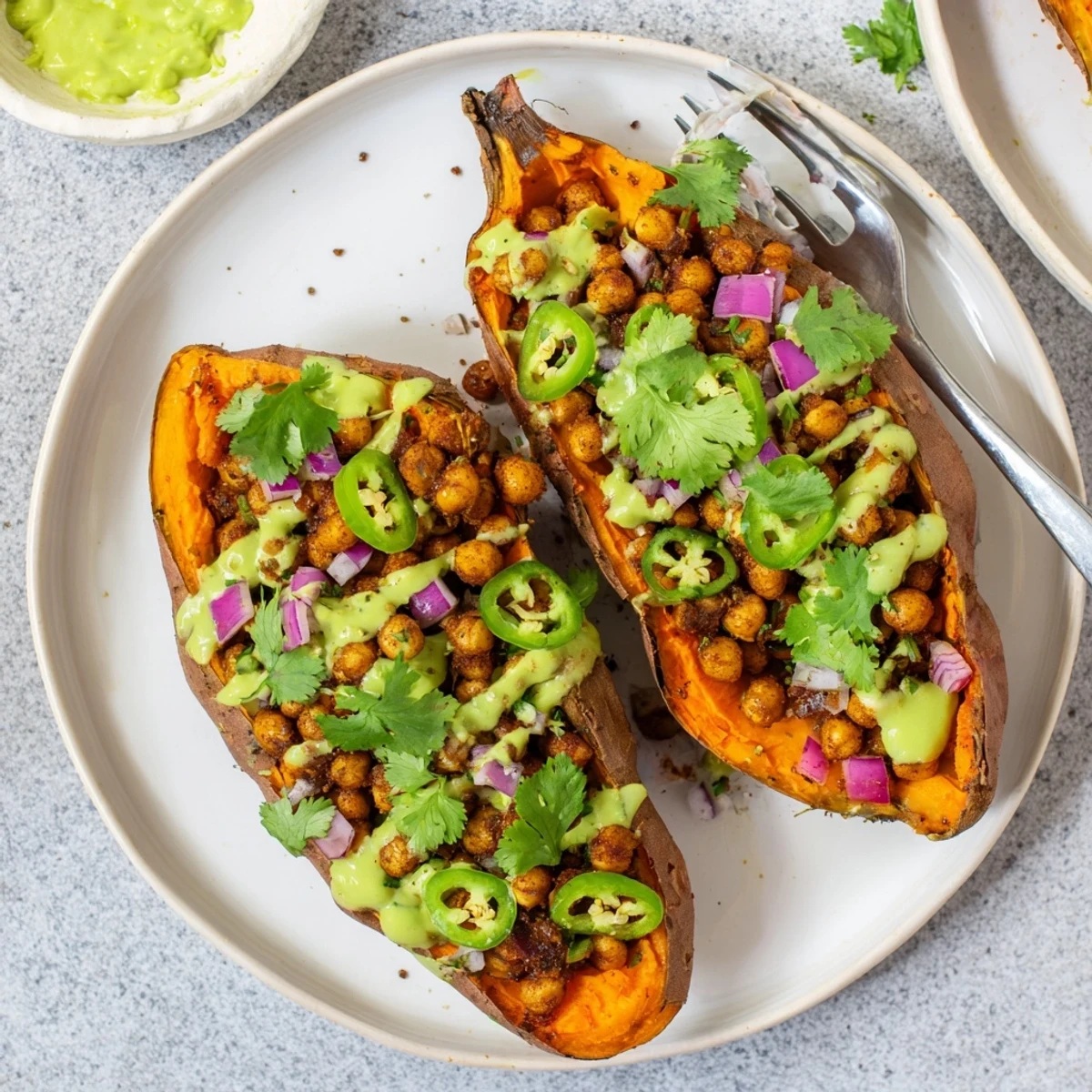 Colorful plate of Vegan BBQ Chickpea Sweet Potatoes topped with red onion and vegan sour cream, perfect dinner.