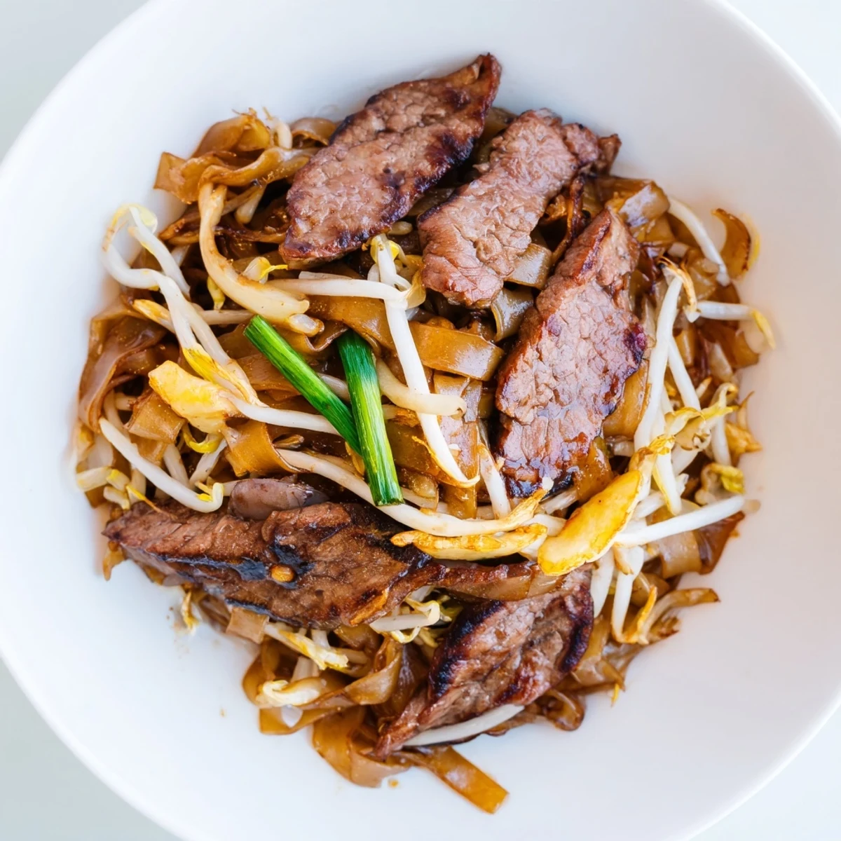 Freshly cooked wide rice noodles are tossed with tender marinated beef, crisp bean sprouts, and green onions in a savory dark sauce in this Beef Chow Fun.