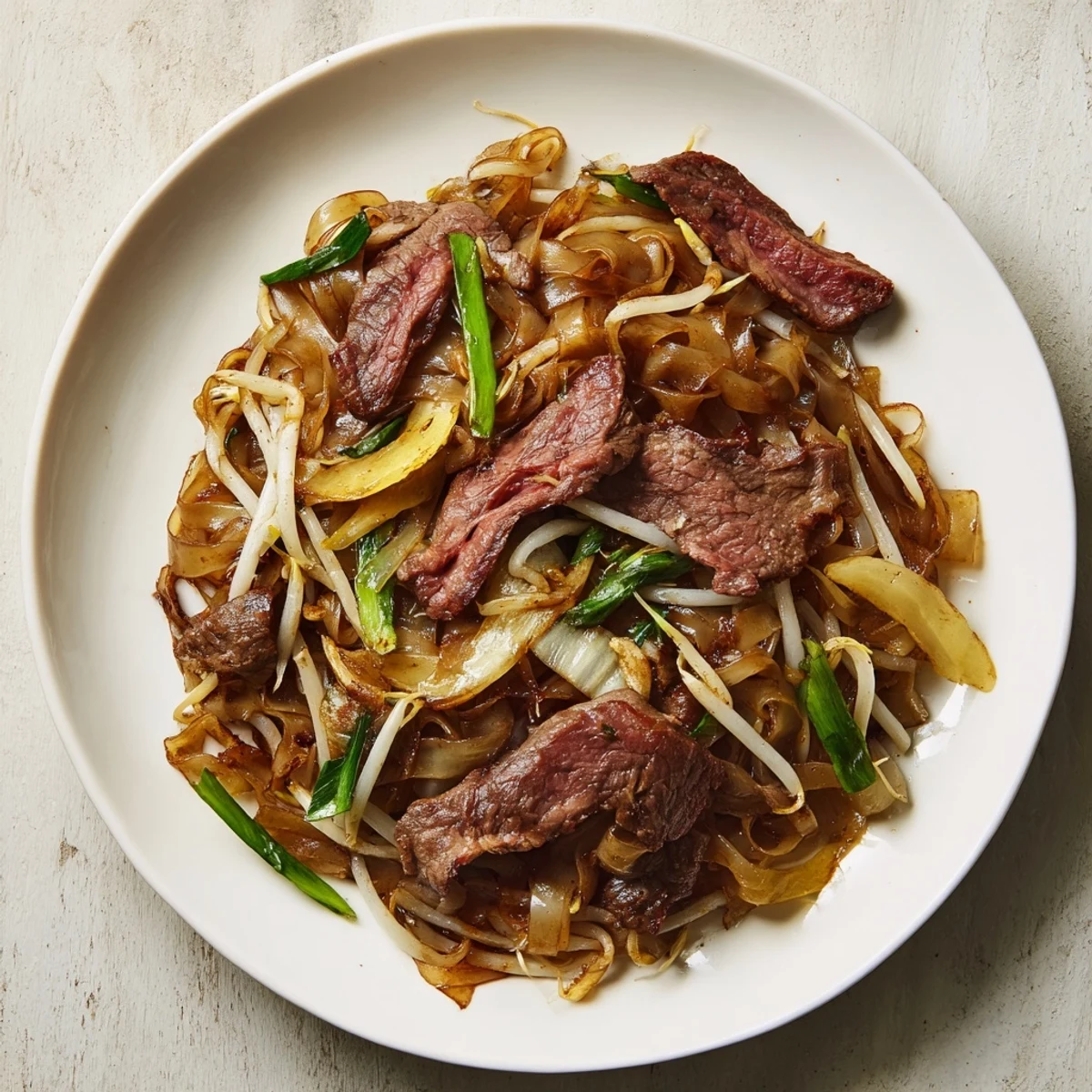 A close-up of sizzling Beef Chow Fun in a hot wok shows charred noodles, caramelized onions, and juicy beef slices ready to serve four people.
