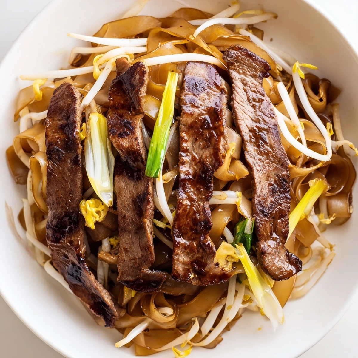 Beef Chow Fun is plated with fresh spring onions garnish on a plate, ideal for a dairy-free Chinese main dish recipe for American home cooks.