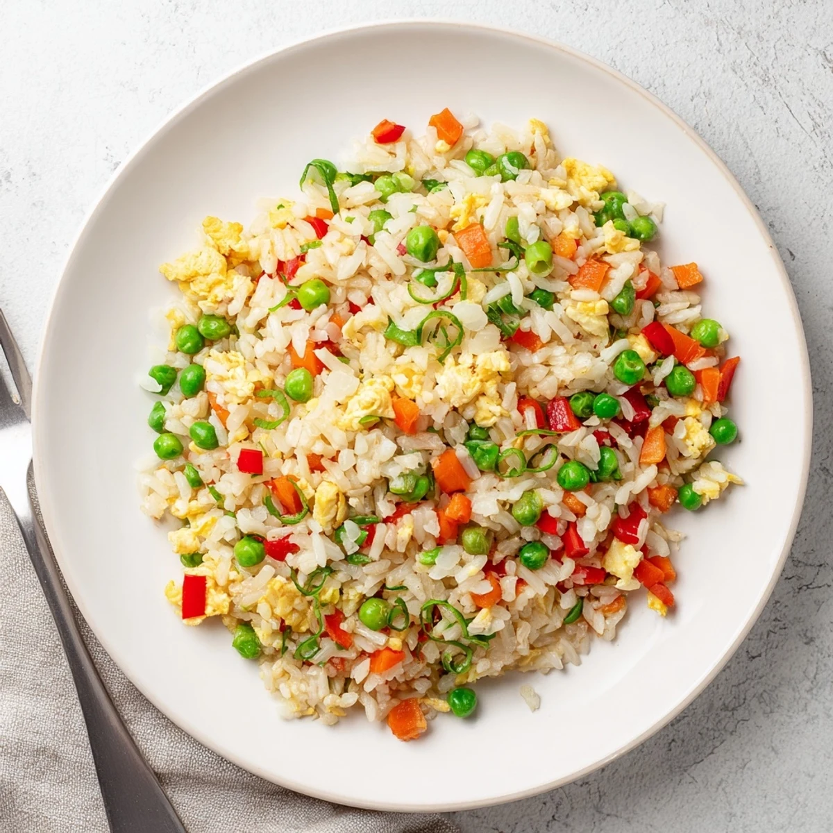 A close-up of vibrant Fried Rice in a white bowl, showcasing fluffy grains, peas, carrots, and fresh green onions.