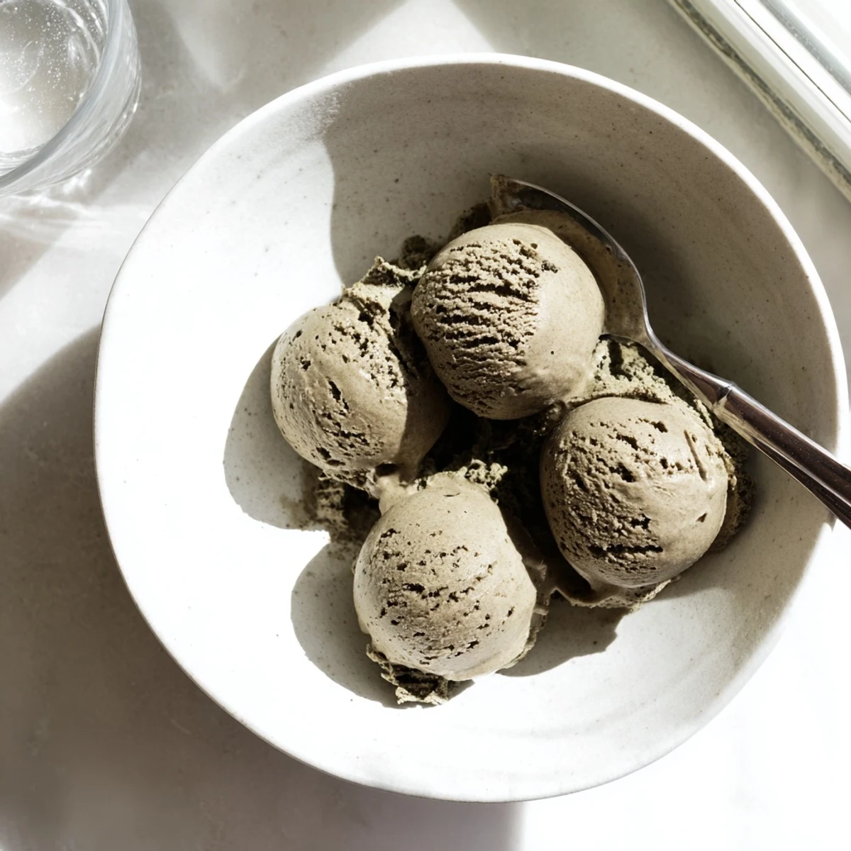 Rich, creamy scoops of Hojicha Ice Cream in a rustic ceramic bowl, topped with toasted sesame seeds.