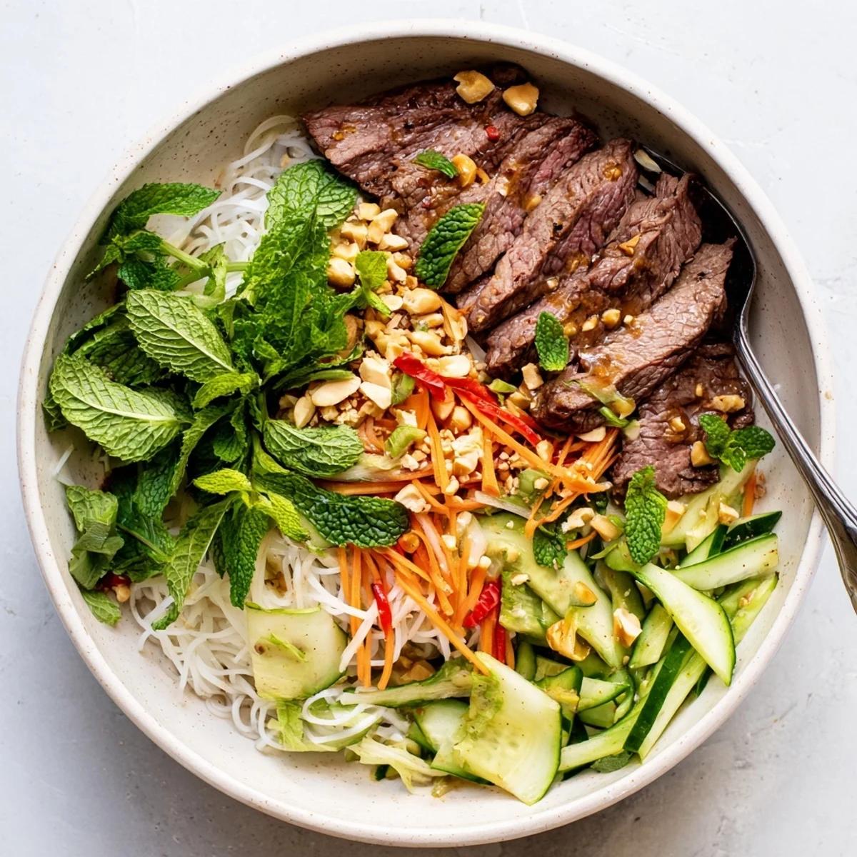 Fresh Bun Bo Xao noodles topped with sautéed beef, crisp carrots, cucumber, and fresh mint leaves.