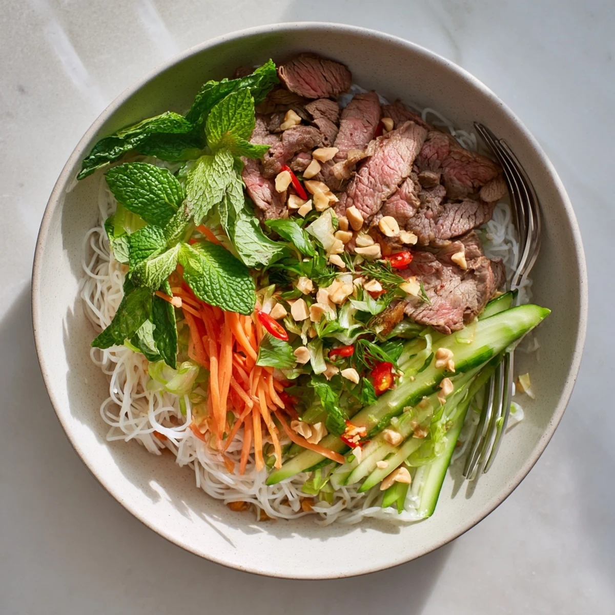 Steaming bowl of Vietnamese noodle salad Bun Bo Xao drizzled with tangy nuoc cham dressing.