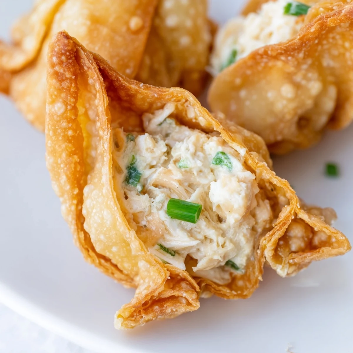Golden fried Crispy Crab Rangoon Bombs stacked high on a plate, revealing creamy filling inside.