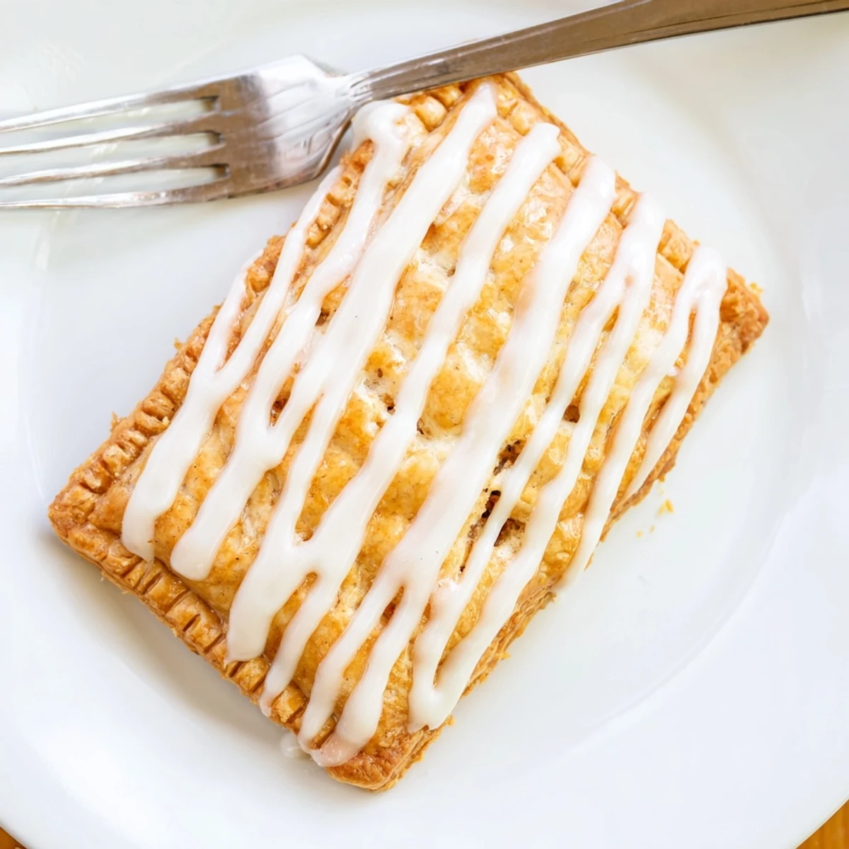 A close-up of Protein Pop Tarts with white icing drizzle, placed on a rustic wooden surface for a cozy breakfast vibe.