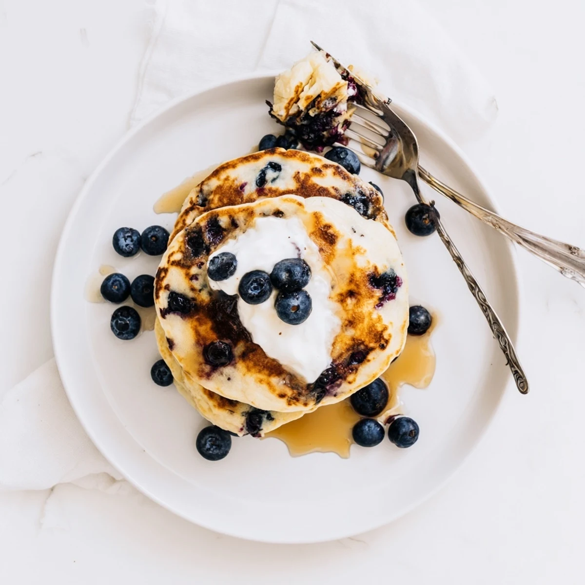Golden Greek Yogurt Blueberry Pancakes stack high with fresh berries and a dusting of powdered sugar on a plate.