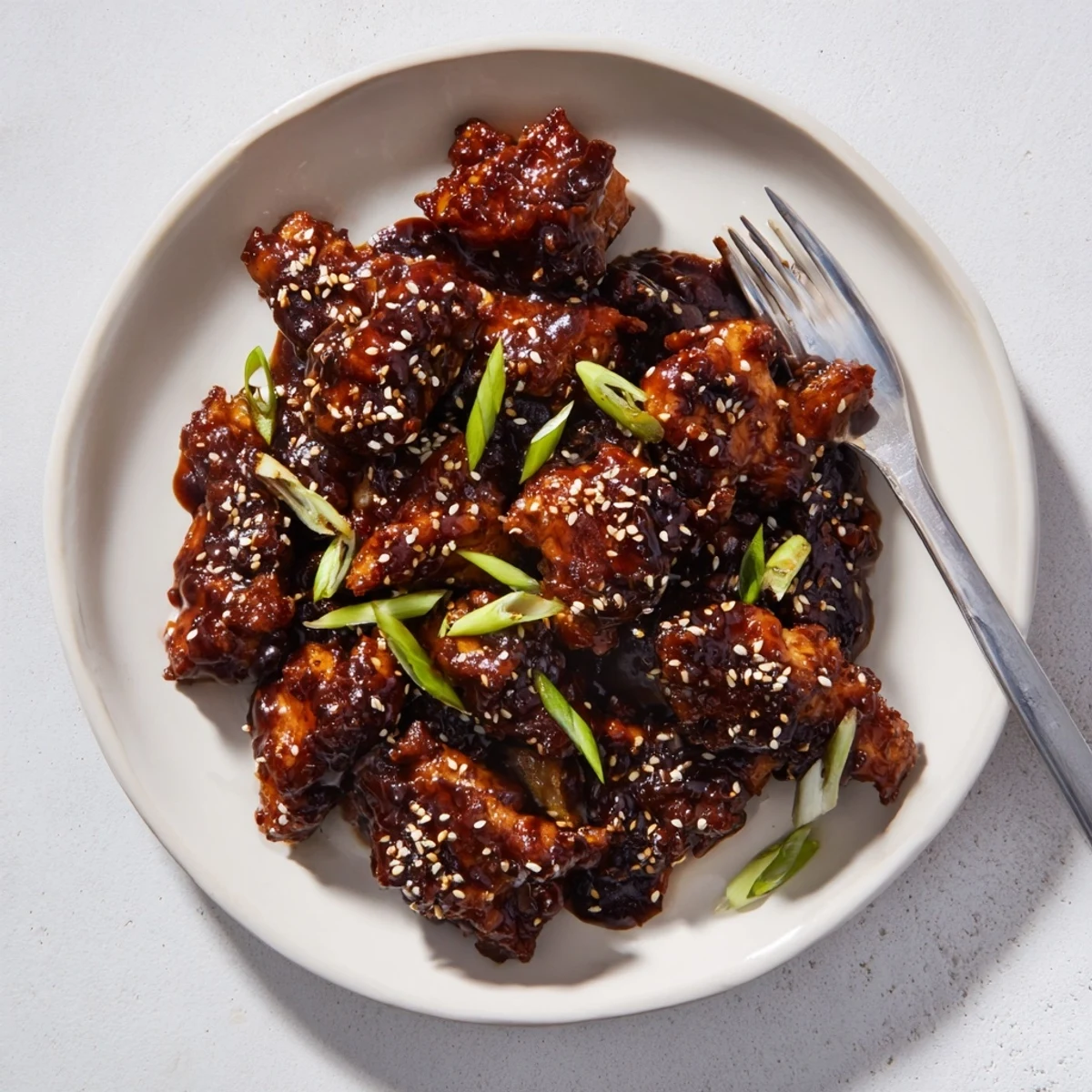 Tender Mongolian chicken pieces coated in rich hoisin garlic sauce garnished with green onions and sesame seeds