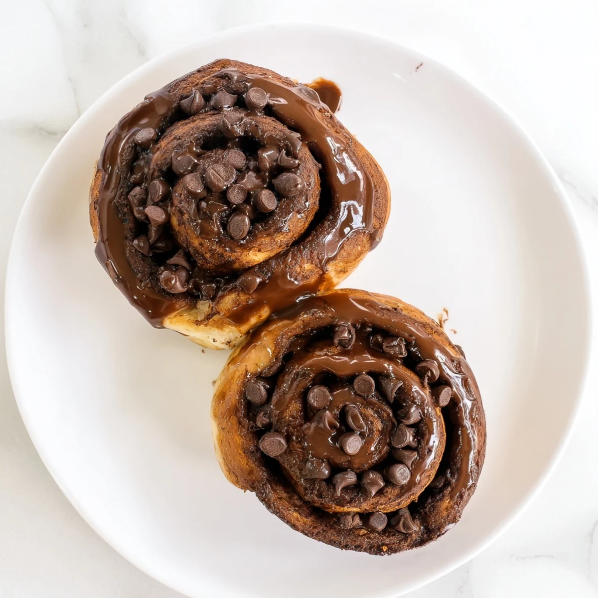 Freshly baked double chocolate cinnamon rolls drizzled with rich chocolate glaze on a white plate