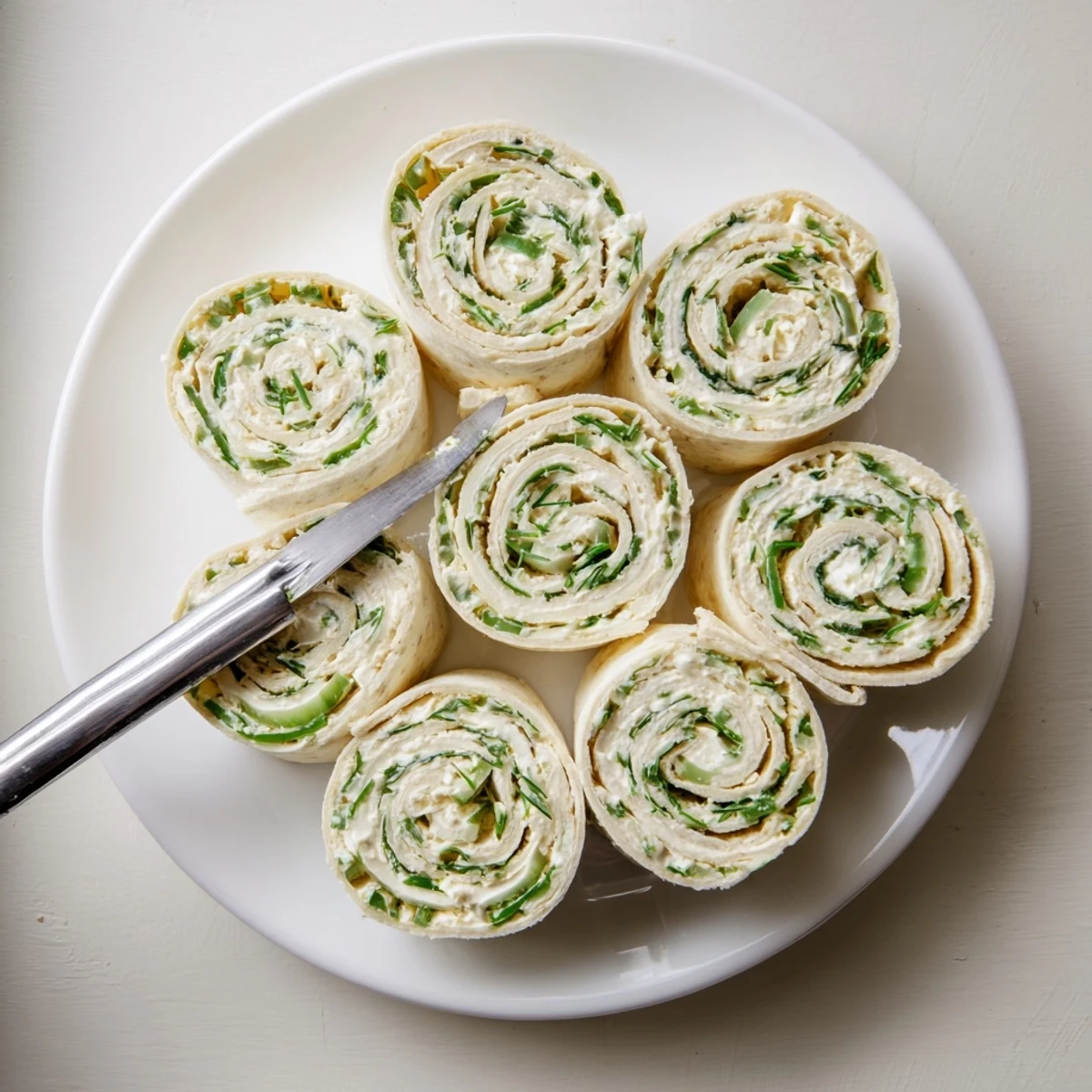 Golden swirls of pickle dip pinwheels arranged on a white serving platter, showcasing green specks of fresh dill and chopped pickles in the creamy cream cheese filling