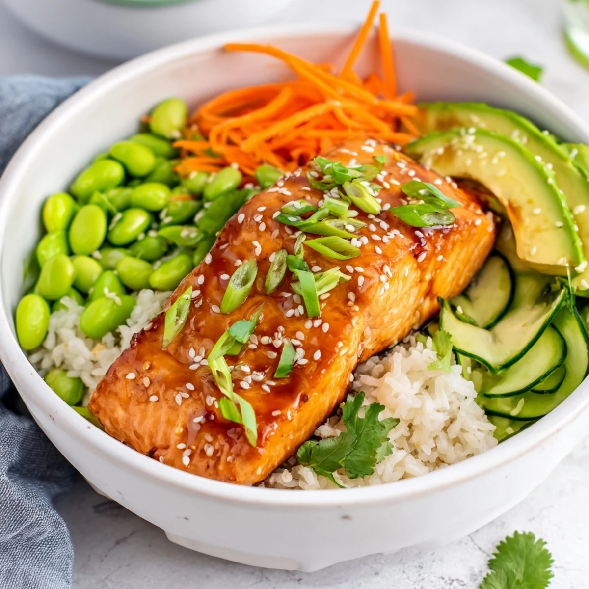 Close up of juicy honey glazed salmon arranged with julienned carrots green onions and creamy avocado slices in this healthy dinner bowl