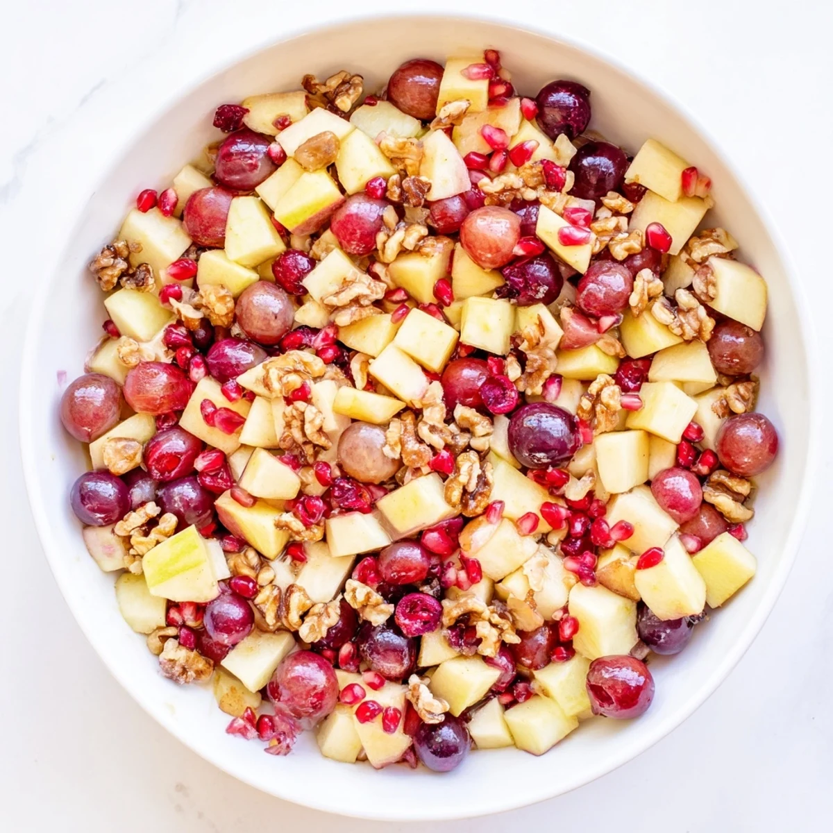 Colorful bowl of minute fall fruit salad with fresh apples, pears, and pomegranate arils tossed in citrus honey dressing
