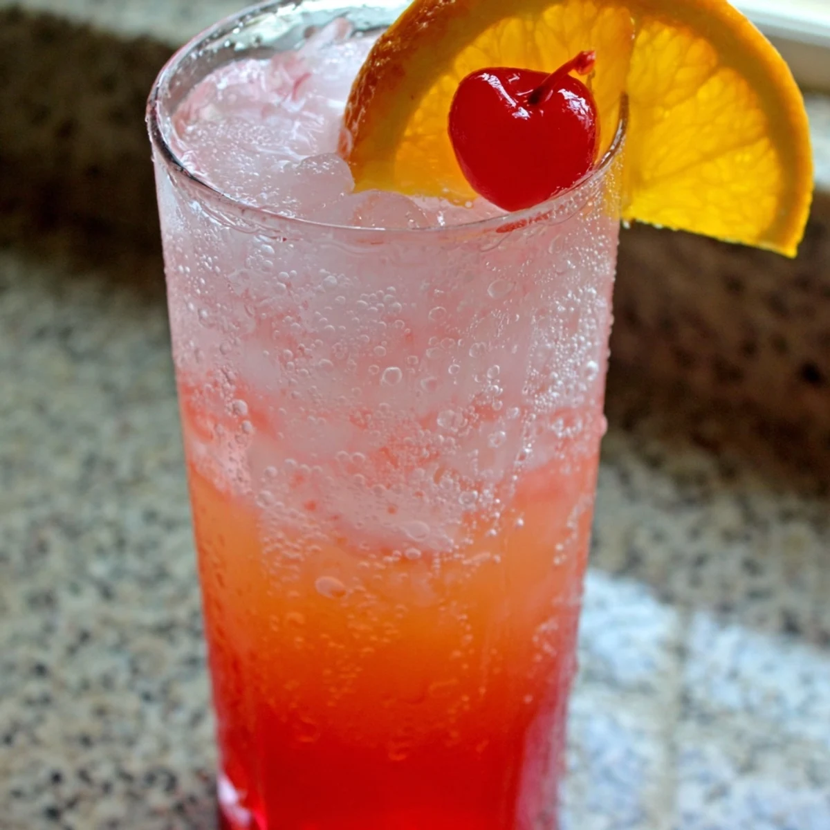 Tall glass of classic Easy Shirley Temple featuring rosy layered soda and orange slice