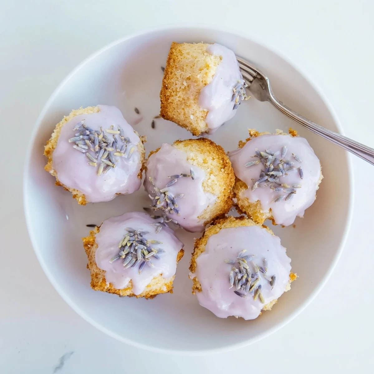 Moist lemon mini cakes topped with lavender-infused glaze and garnished with fresh lemon zest