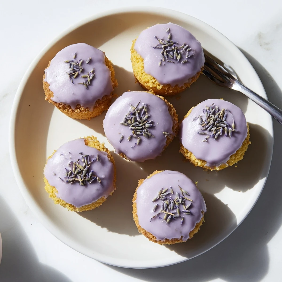 Golden mini lemon cakes drizzled with fragrant purple lavender glaze on a white serving plate