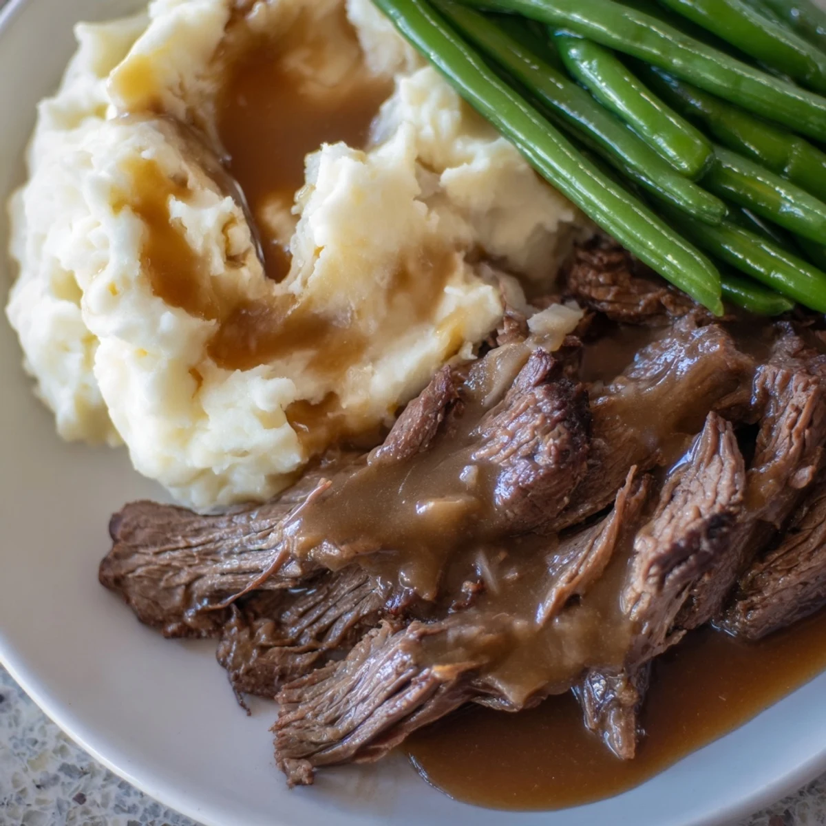Golden brown Southern style pot roast plate with tender beef slices beside fluffy mashed potatoes and bright green beans