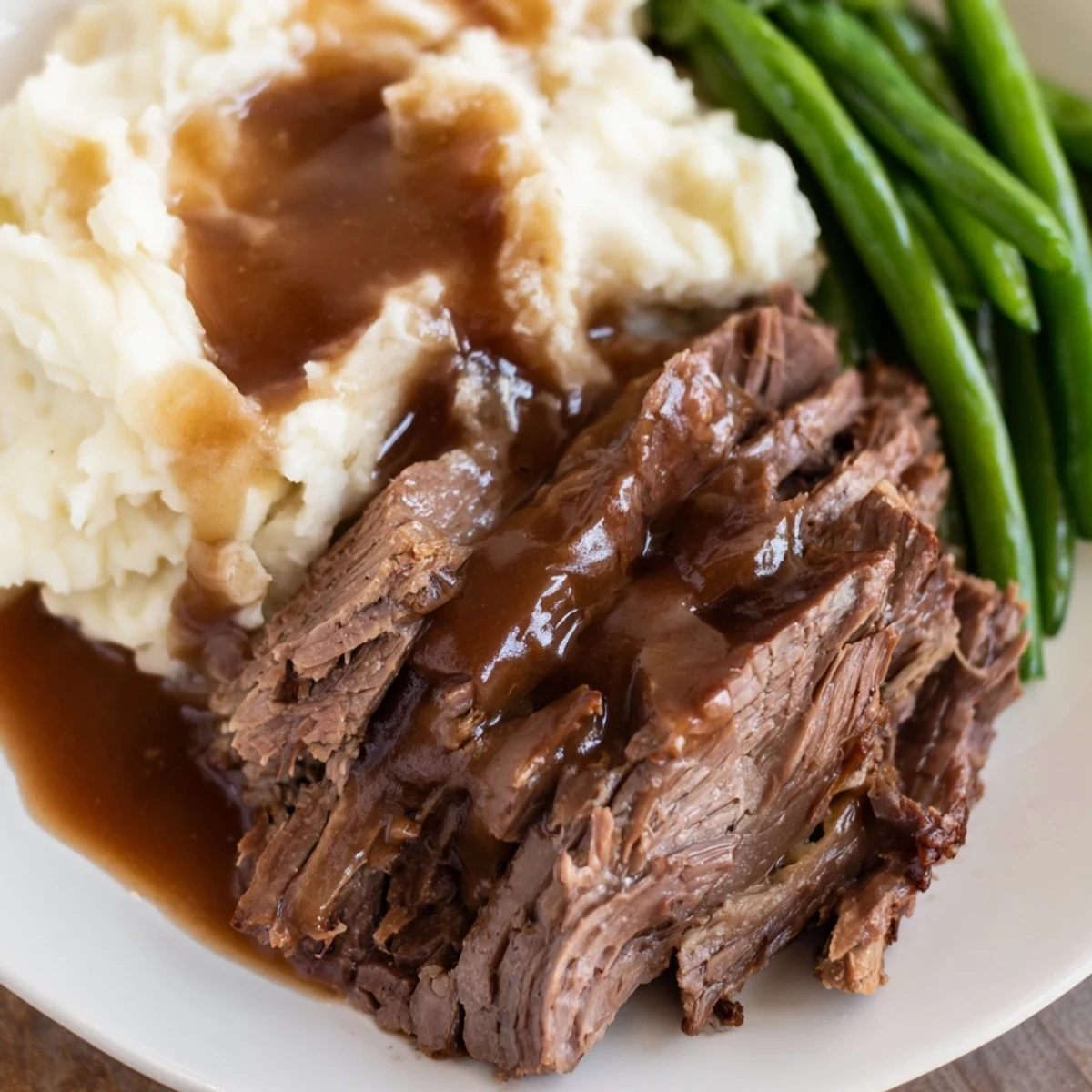 Complete Southern style pot roast plate featuring fork-tender beef chunks with roasted vegetables and seasoned green beans on white ceramic dish