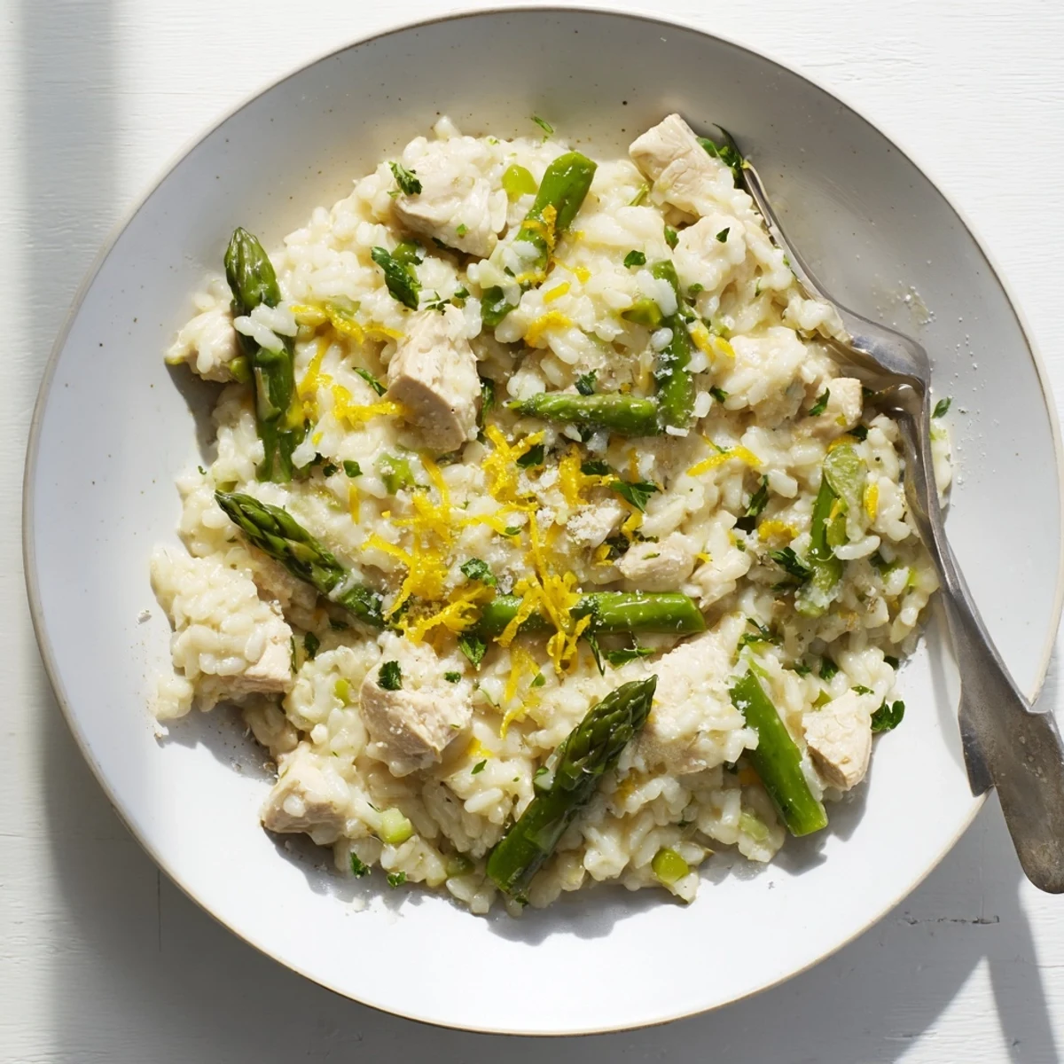 Creamy chicken and asparagus risotto topped with grated Parmesan and fresh parsley in a white bowl