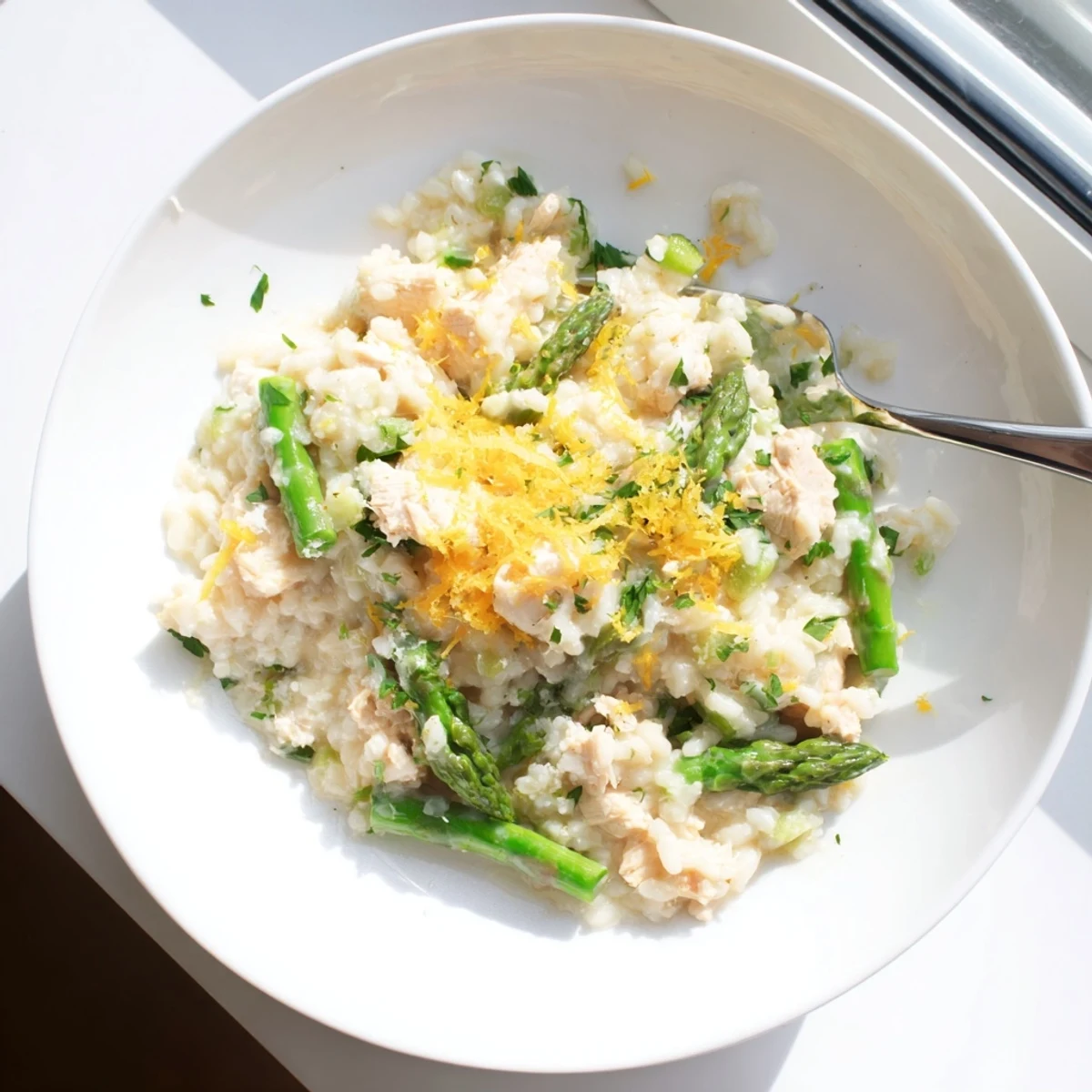Spoonful of lemon-infused chicken and asparagus risotto garnished with extra Parmesan cheese on a rustic wooden table