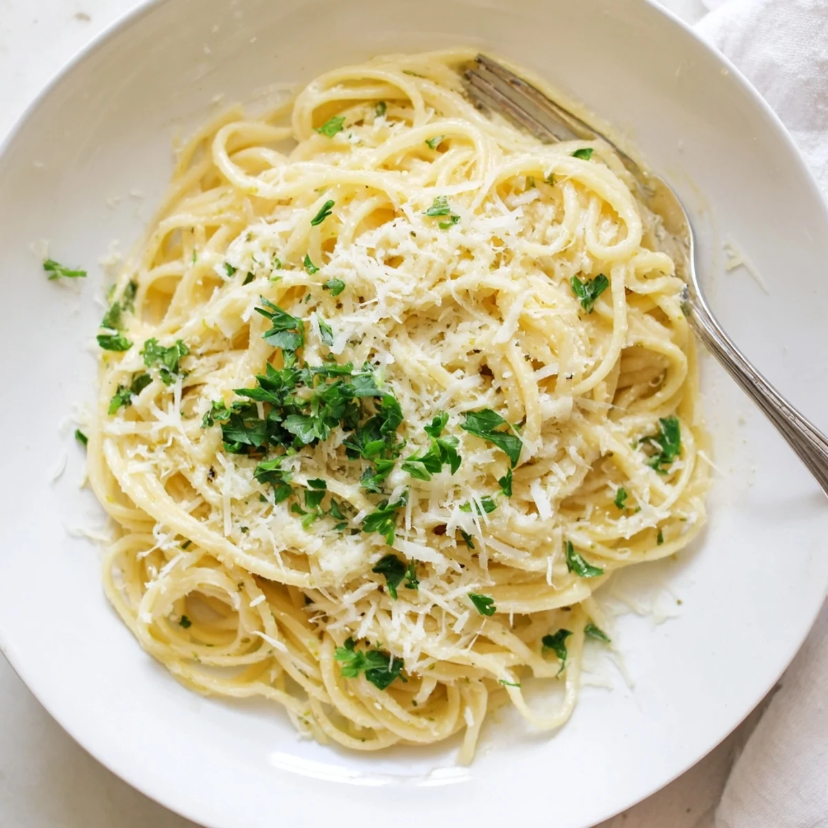 Close up of one pot garlic butter pasta with grated parmesan and lemon zest on white ceramic bowl