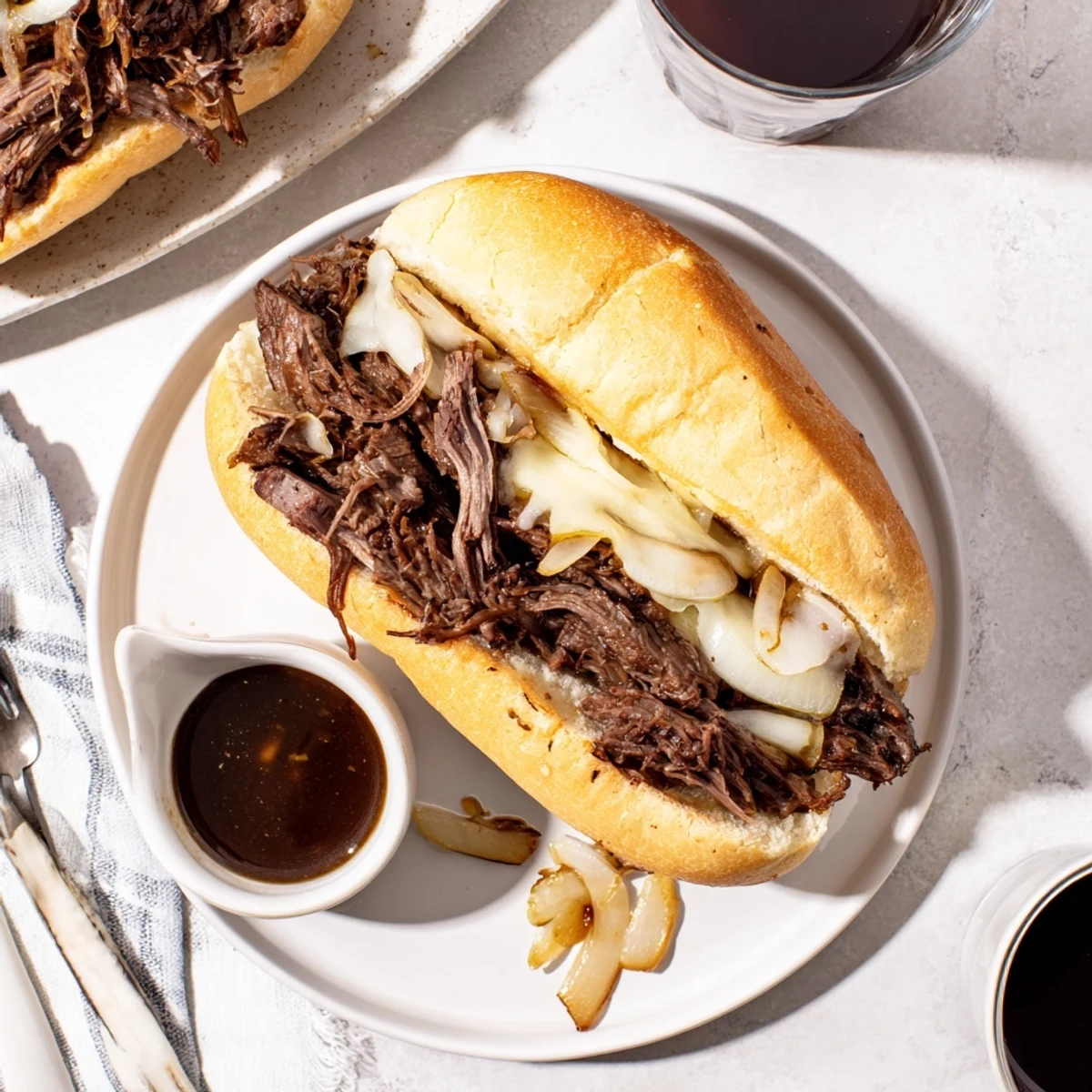 Slow-cooked chuck roast shredded and served on crusty bread alongside a small bowl of rich savory au jus for dipping