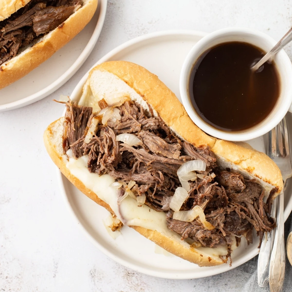 Tender beef sandwich overflowing onto a toasted roll with melted cheese slice, ready to dunk into flavorful broth from the Crockpot French Dip Sandwiches recipe