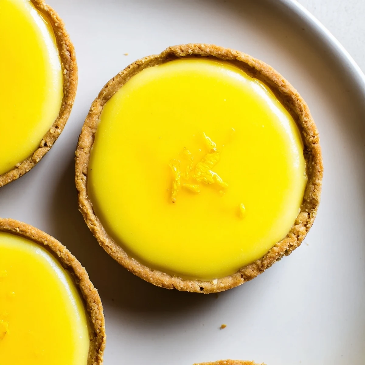 Creamy vegan lemon tarts in golden almond crusts garnished with delicate lemon zest