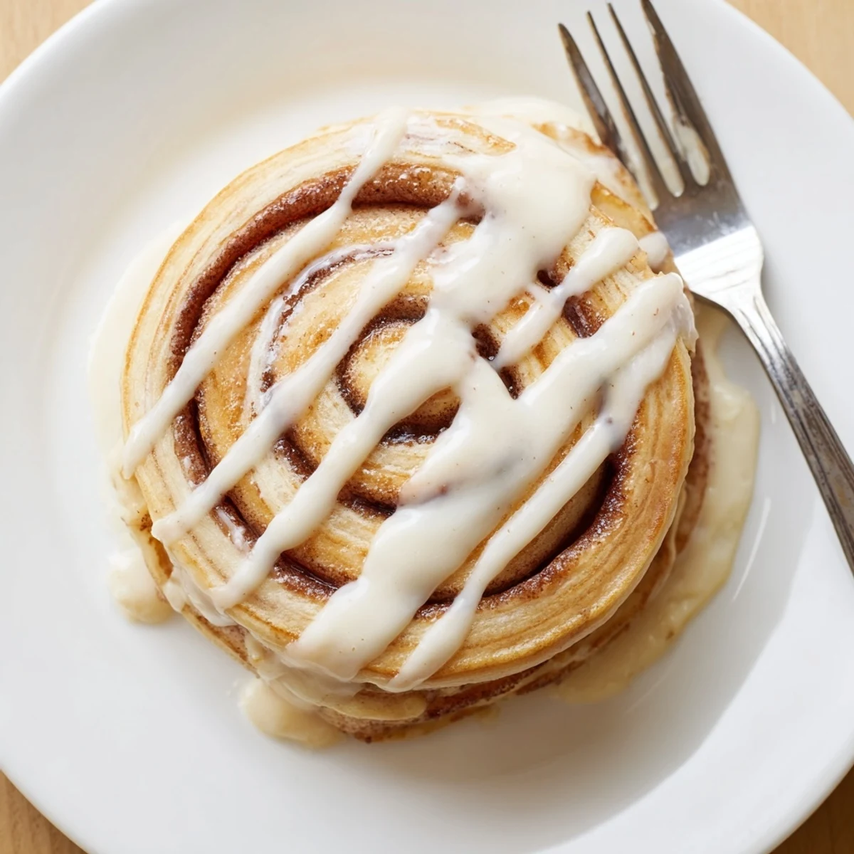 Golden cinnamon roll pancakes stacked high with creamy cream cheese icing drizzled on top