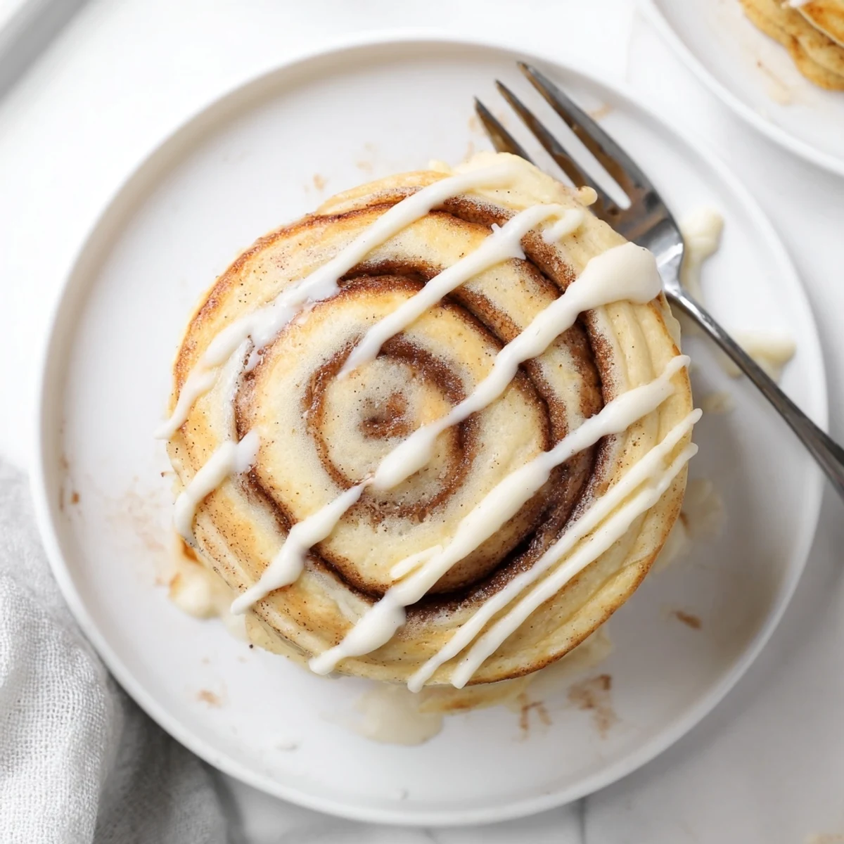 A stack of cinnamon roll pancakes dripping with sweet icing alongside a pat of butter