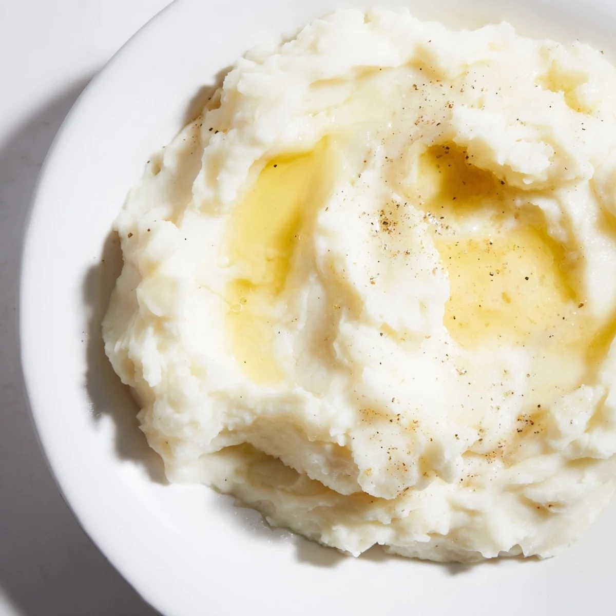 Creamy mashed potatoes topped with melting butter in a white serving bowl