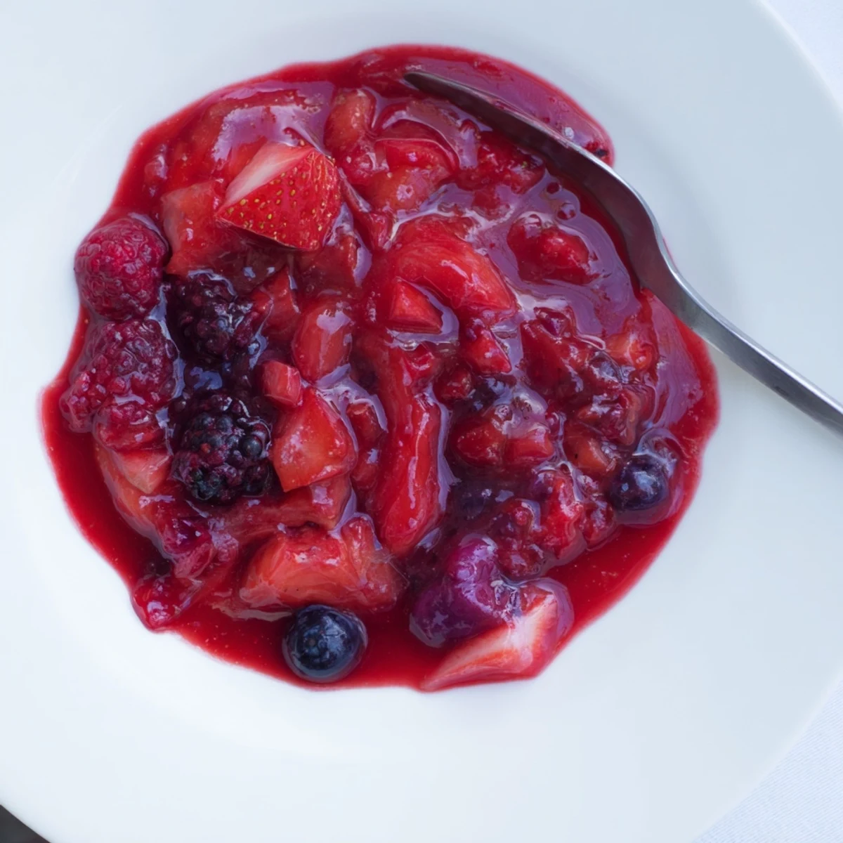Rustic mason jar filled with vibrant strawberry rhubarb raspberry jam garnished with whole strawberries