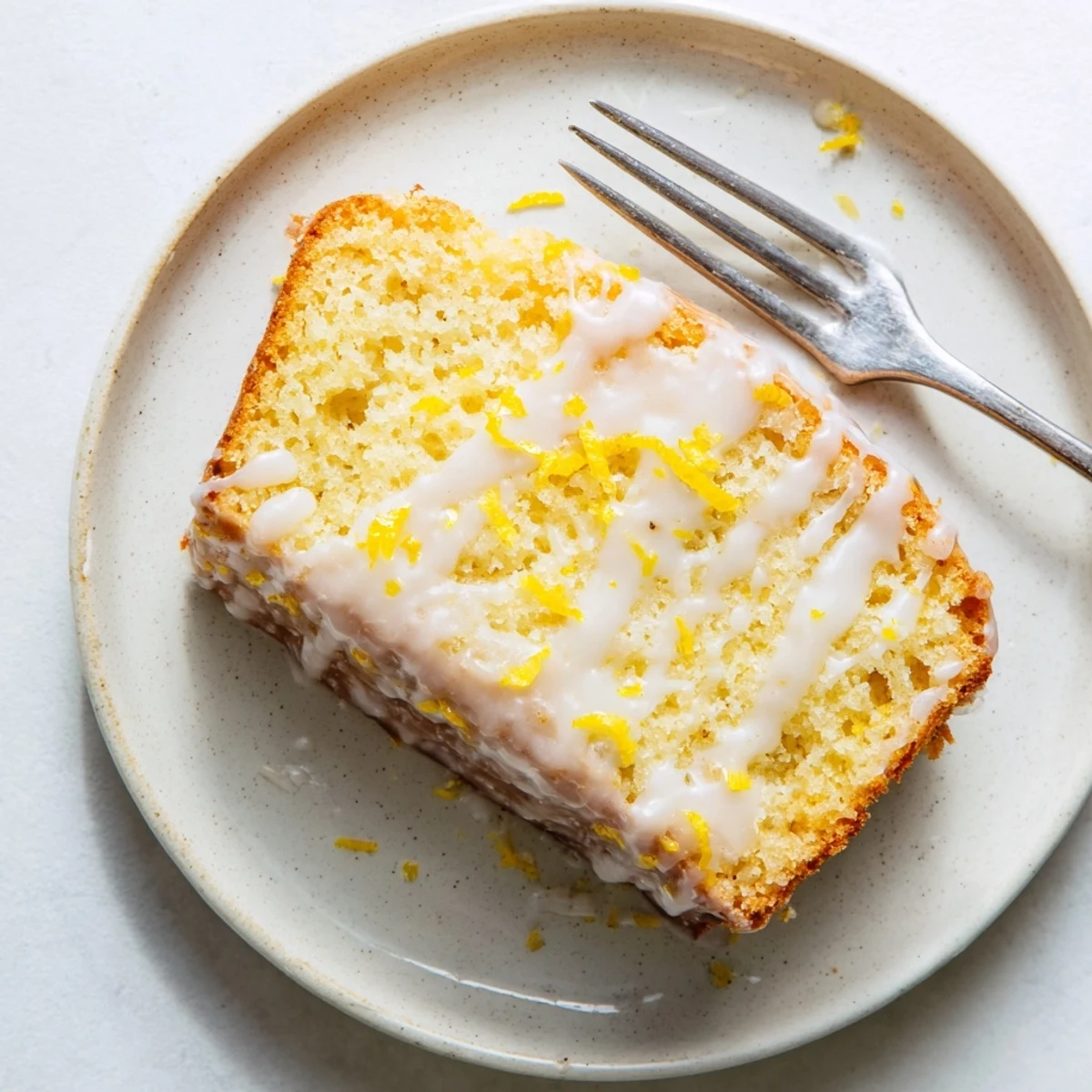 Golden brown Greek yogurt lemon loaf drizzled with white glaze on a wooden cutting board